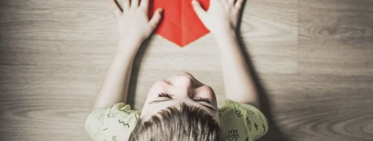 Photo of child holding red paper heart.