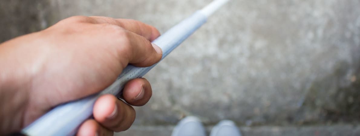 Photo of man holding cane, looking down at feet.