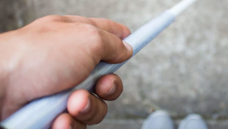 Photo of man holding cane, looking down at feet.
