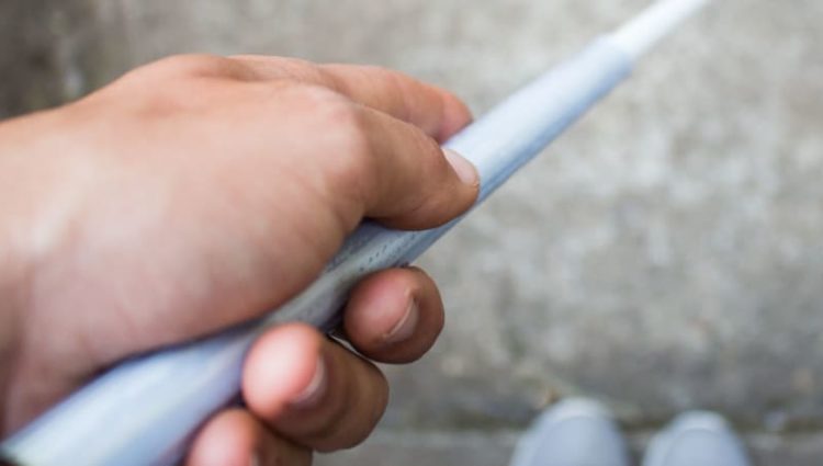 Photo of man holding cane, looking down at feet.