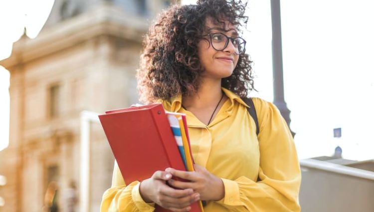 Photo of young female student carrying study materials.