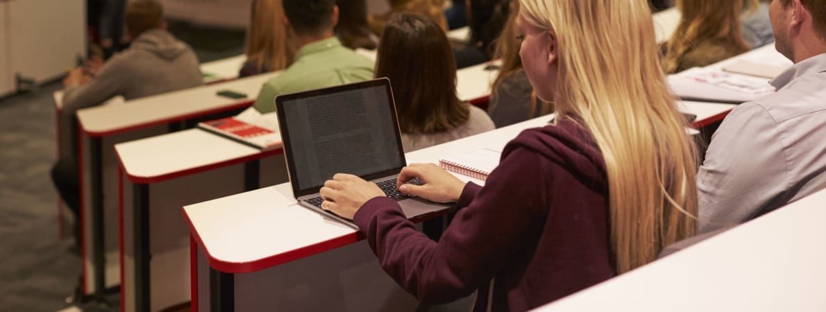 Photo of woman typing on laptop in lecture hall.