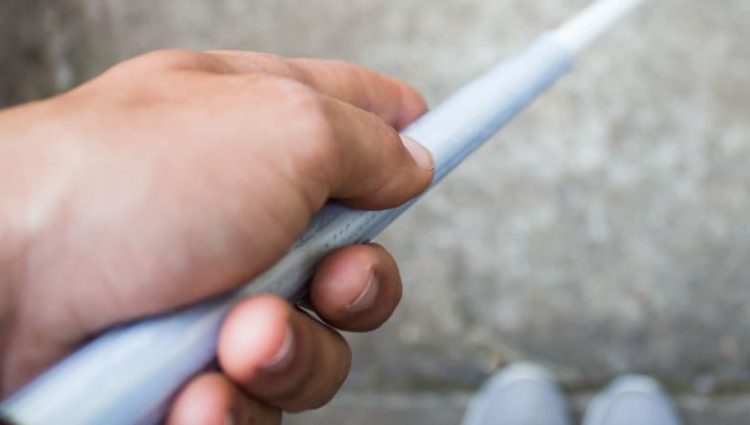 Photo of man holding cane, looking down at feet.