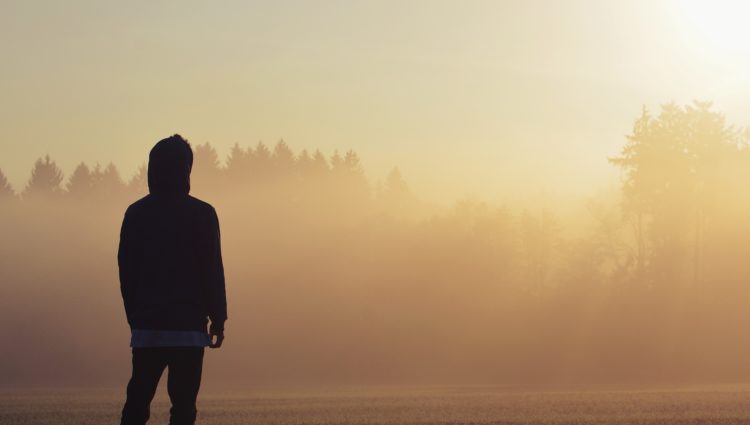Teenage boy facing away from the camera. The sun is setting behind him