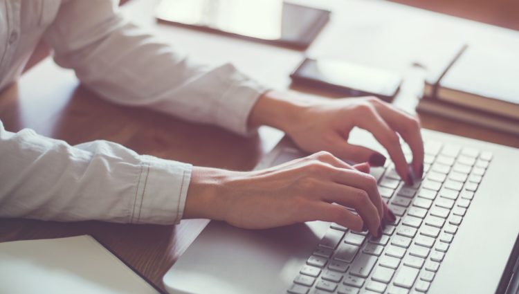 Close up of womans hands typing on a laptop