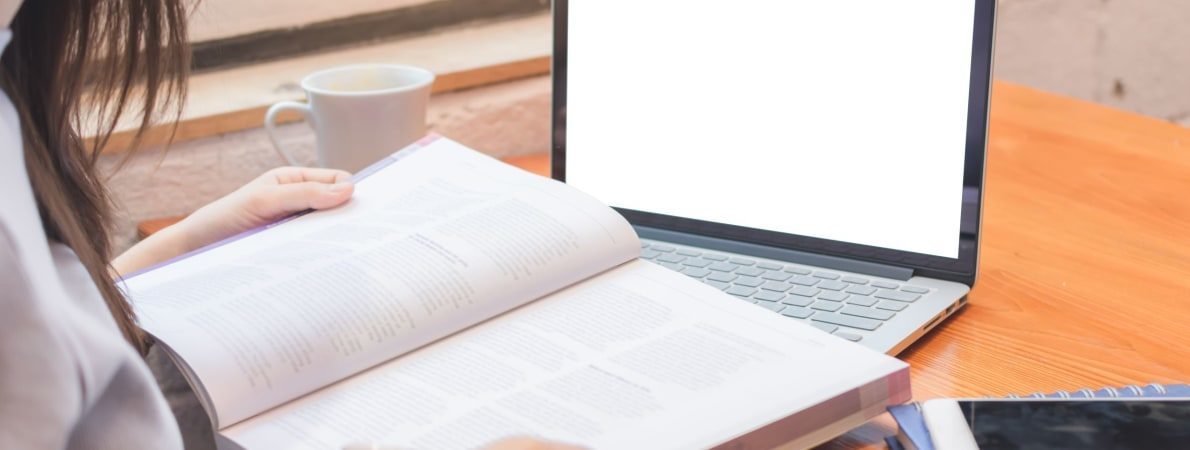 Person reading a book with laptop on desk