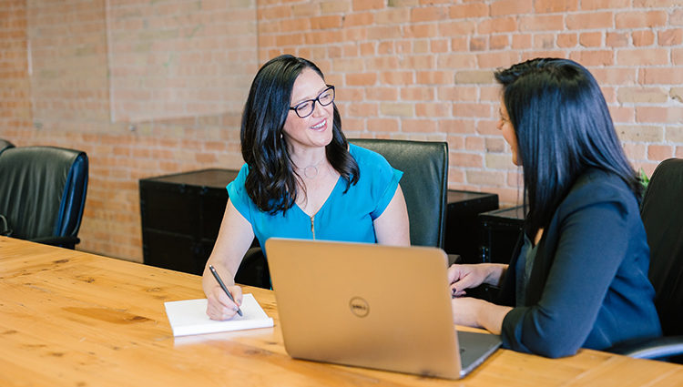 Two women sat at a boardroom table smiling at each other