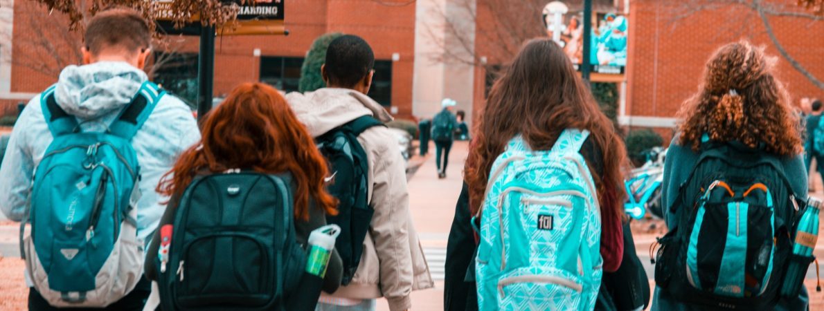 Five students walking to college with backpacks on.