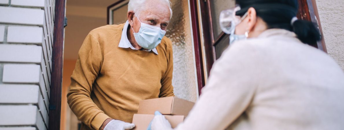 Elderly man receiving home delivery. Both people wear masks.