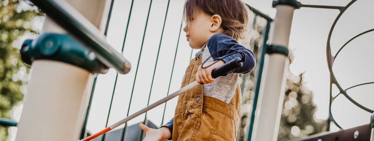Child with white cane on play equipment