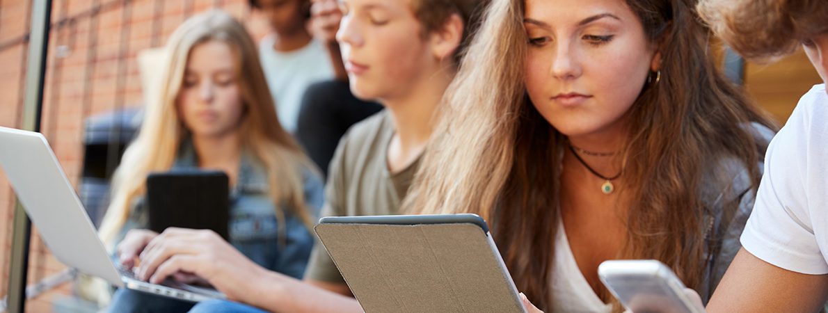 A group of students sitting on a bench using Ipads and laptops