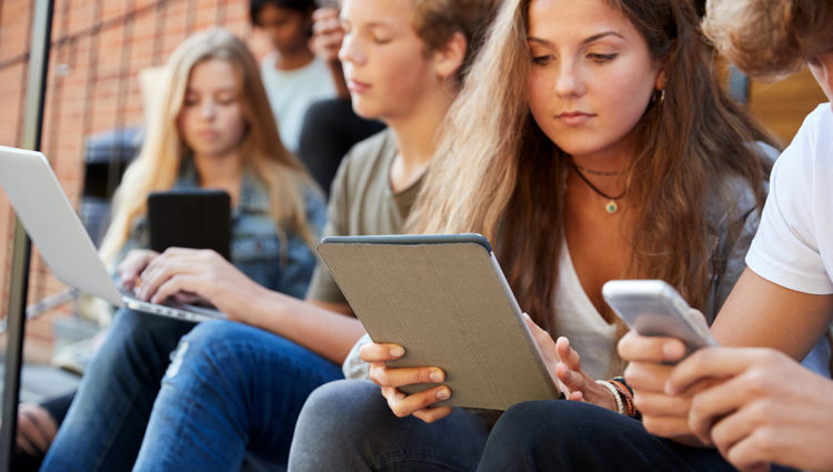 A group of students sitting on a bench using Ipads and laptops