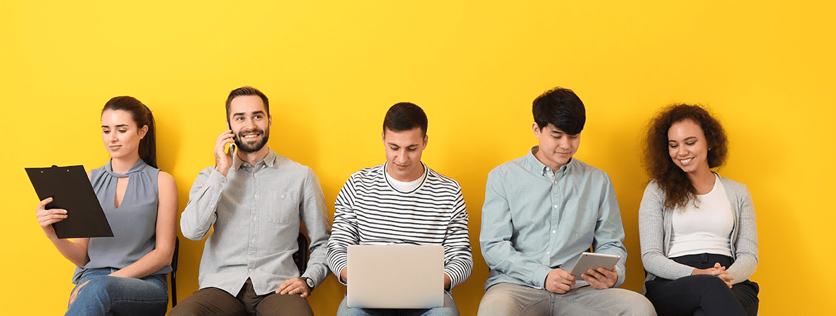 Five young people sat on chairs in a row in front of a bright yellow wall.