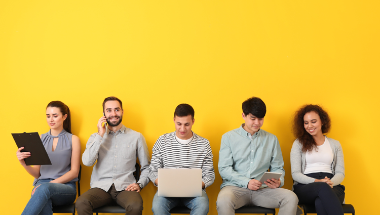 Five young people sat on chairs in a row in front of a bright yellow wall.
