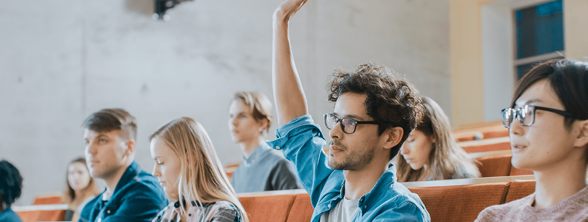 Young man with hand up in a university lecture theatre