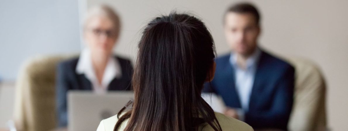 Interview photograph showing back of interviewees head and two people opposite her in suits