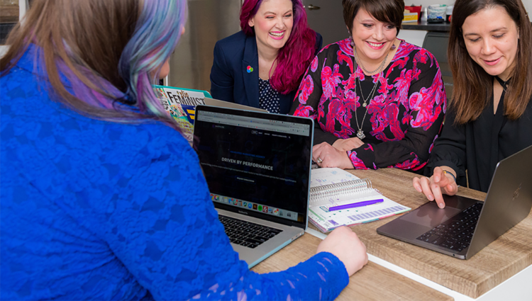 Four women dressed in business wear looking at the same laptop