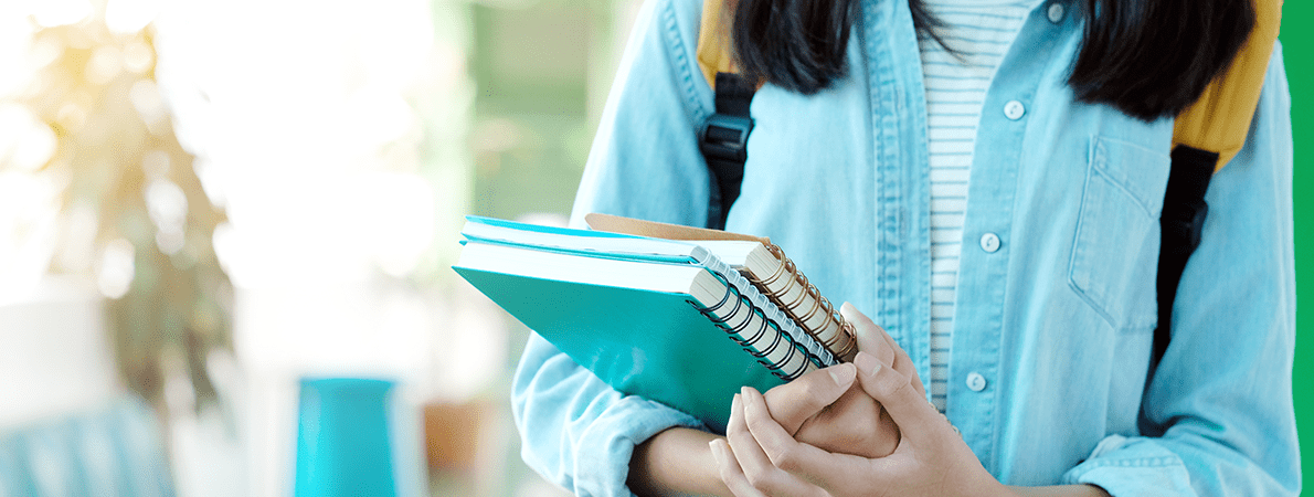 A close up of a female student holding a stack of notepads, walking down a university corridor