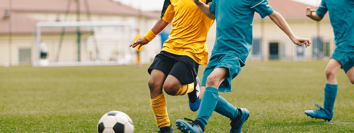 A close up of young people playing football. One is in a yellow football strip, the other is in blue.