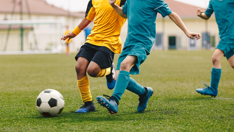 A close up of young people playing football. One is in a yellow football strip, the other is in blue.