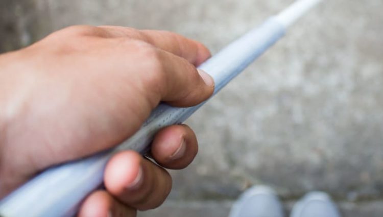 Photo of person holding walking cane, looking down at feet.