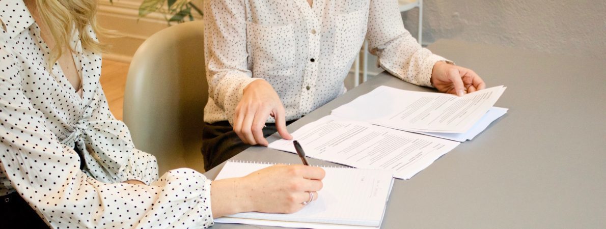 Two women sat at a desk writing on a stack of paper