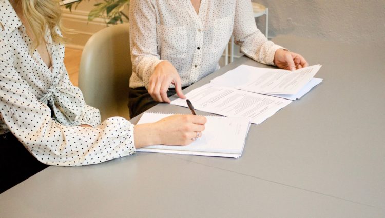 Two women sat at a desk writing on a stack of paper