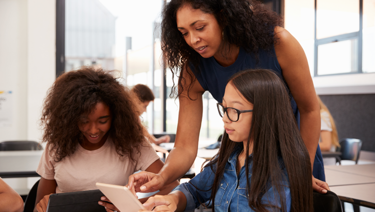 Teacher leaning over table talking to two young female students