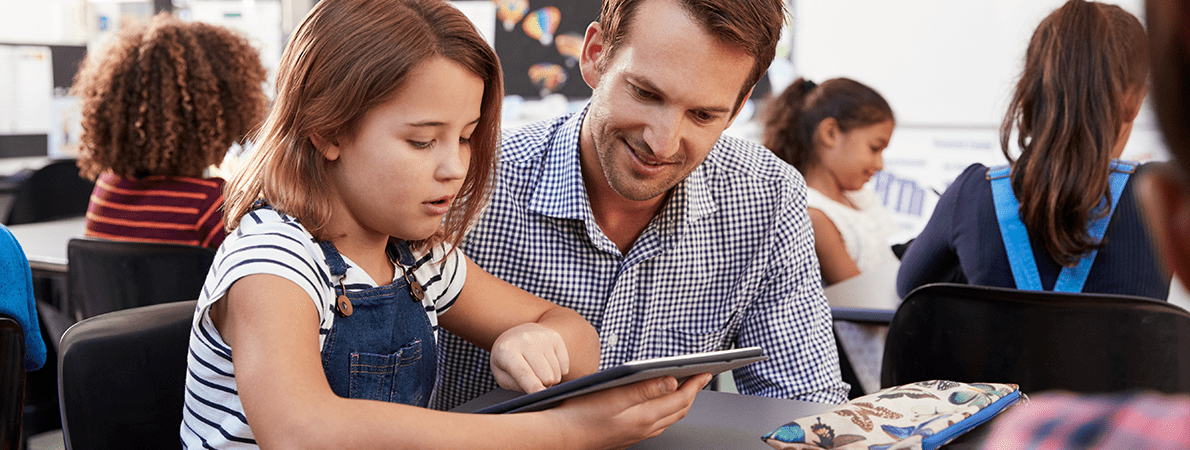 Teacher and young schoolgirl using tablet in classroom