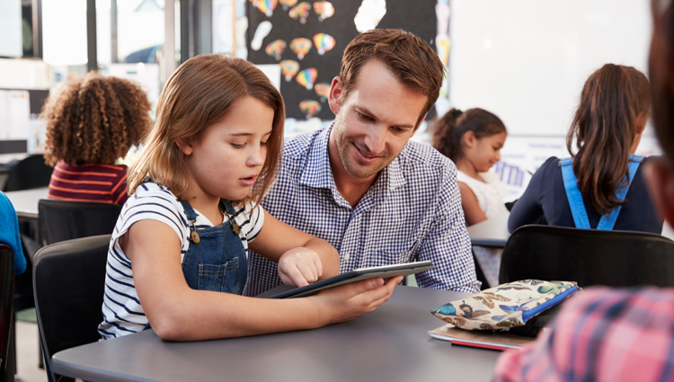 Teacher and young schoolgirl using tablet in classroom