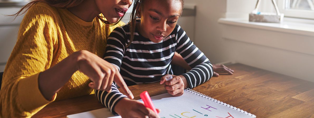 Woman teaching young girl the alphabet at a desk