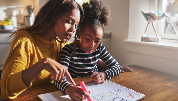 Woman teaching young girl the alphabet at a desk