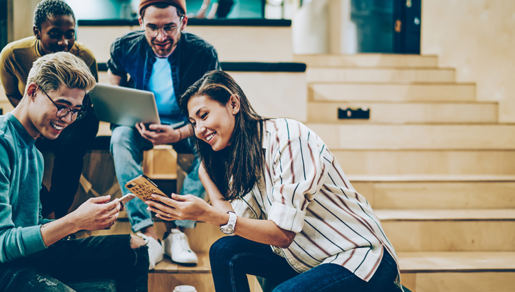 Four young people chatting smiling sharing laptops
