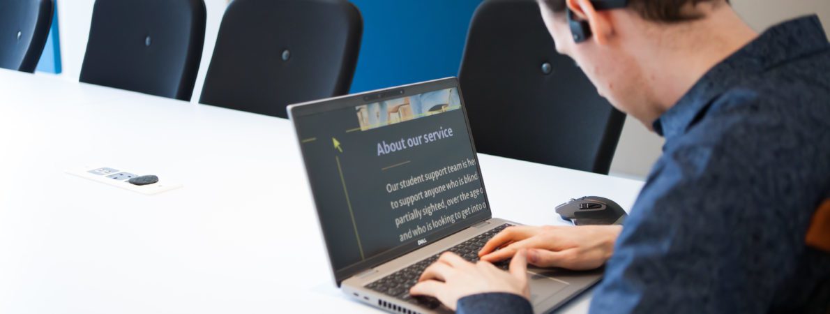 Blind man using zoom text on a laptop in a meeting room