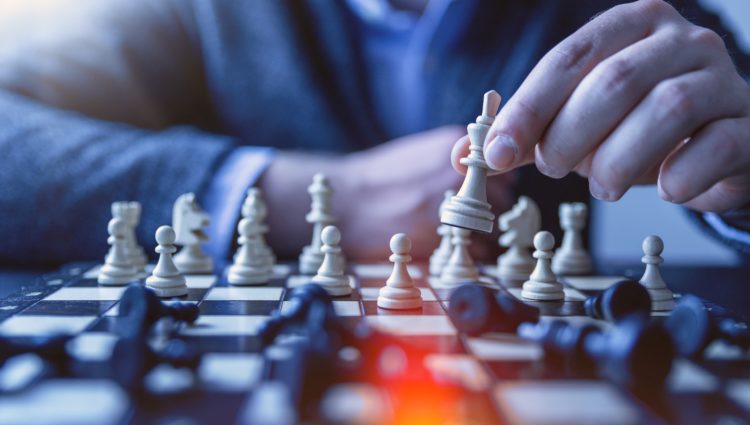 A man sat behind a chess board, moving a piece