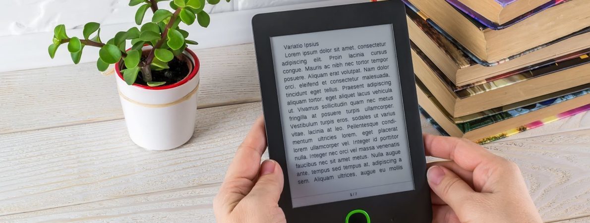 Person holding a tablet with a text, on a desk, with some books and a plant on it