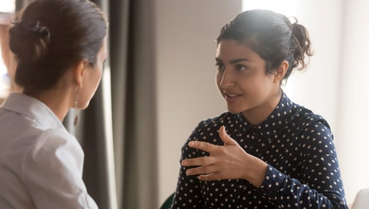 a woman in a white top is talking to another woman with a black spotty top, who is listening to what the first woman is saying.