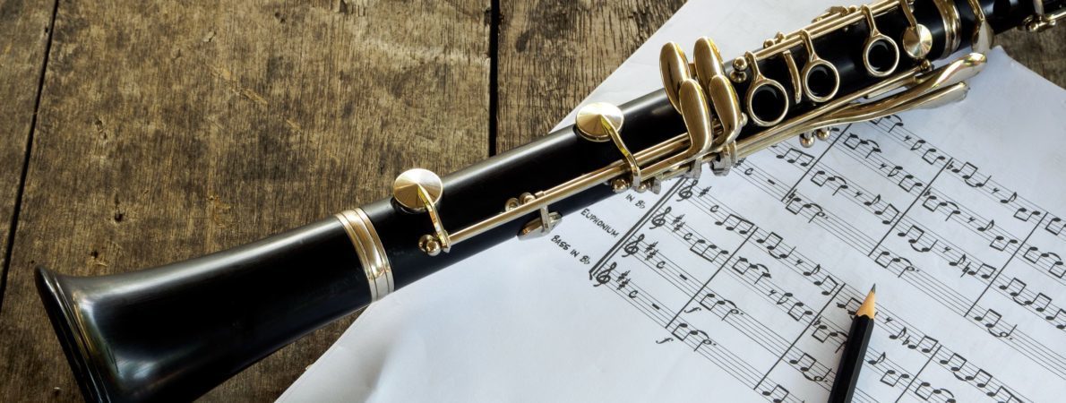 Close up picture of a clarinet on a wooden table, some music sheets and a pencil