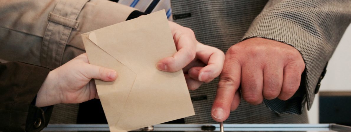 A ballot paper is being inserted into a ballot box.