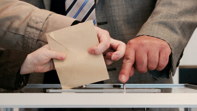 A ballot paper is being inserted into a ballot box