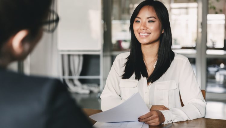 a woman sitting on a table opposite to a man, holding papers and smiling