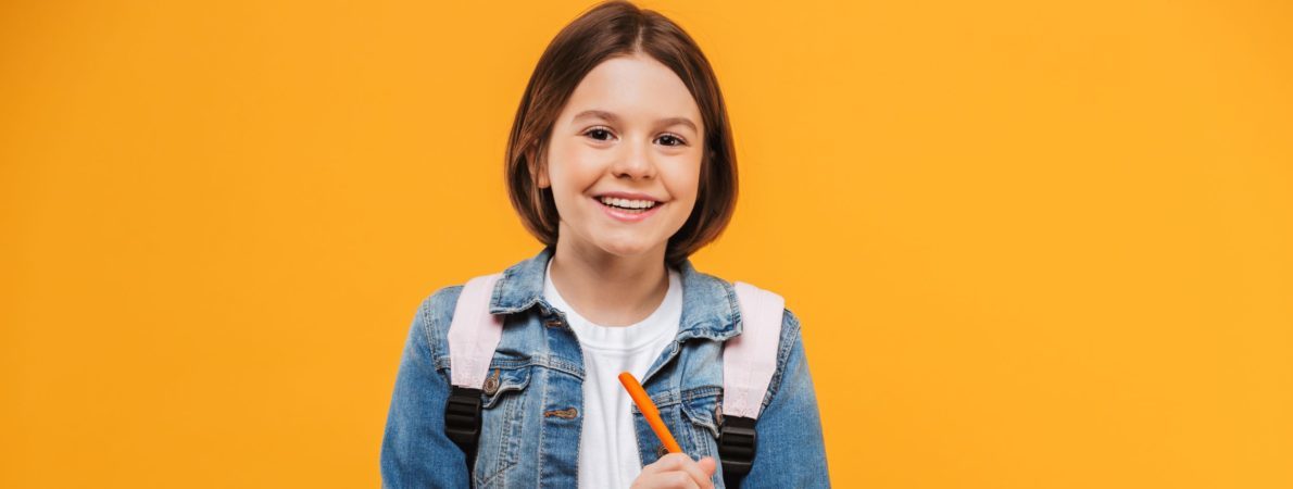 A young girl, holding some books and taking notes while smiling at the camera