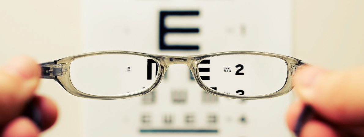 A close up picture of a pair of glasses, held by someone, and a board with letters at the background