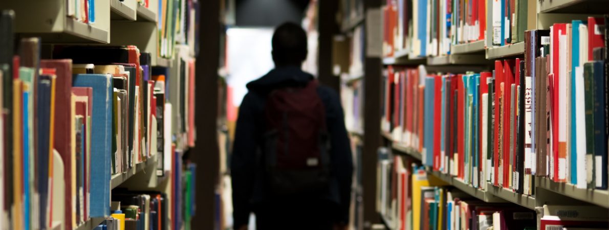 A man walking in a library full of books on the shelves