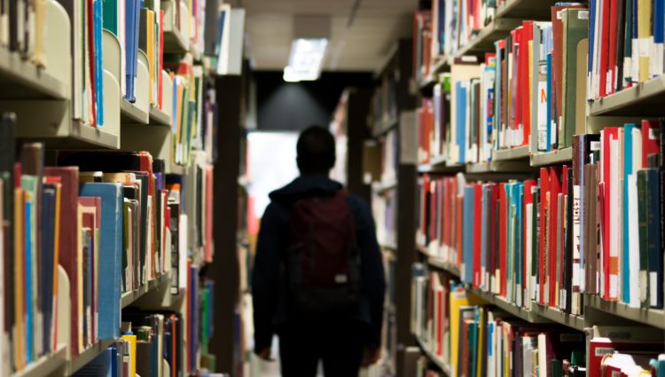 A man walking in a library full of books on the shelves