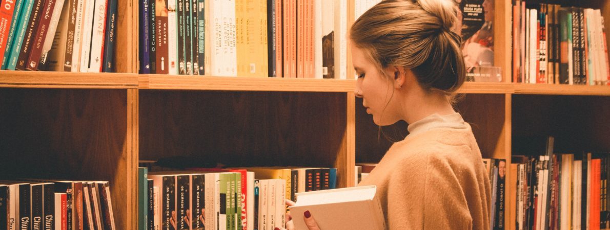 A young woman holding a book looking for a book in a library