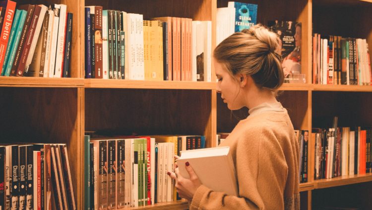 A young woman holding a book looking for a book in a library