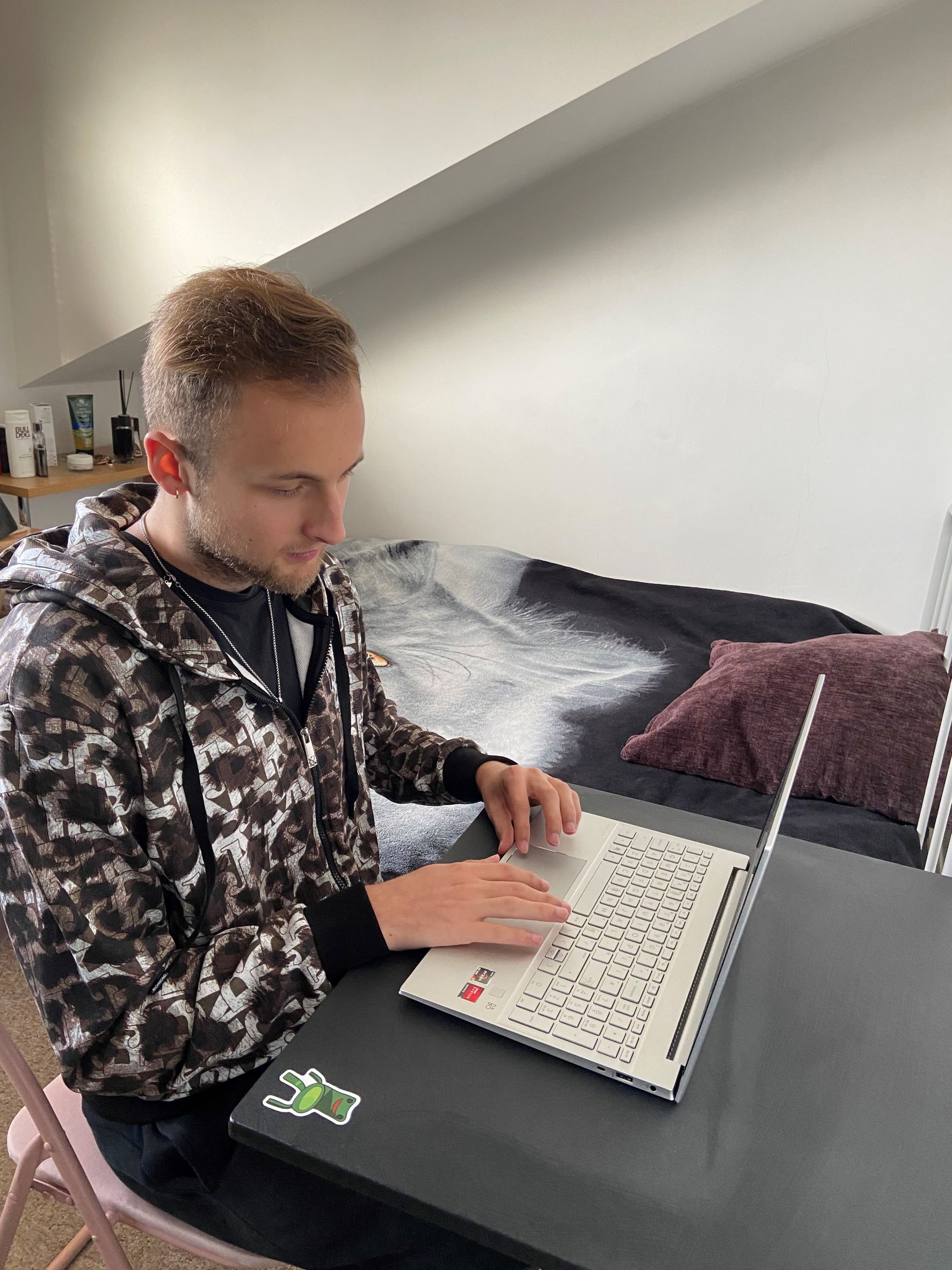 A picture showing Aleksandr studying in front of his laptop, sat on a desk in his bedroom.