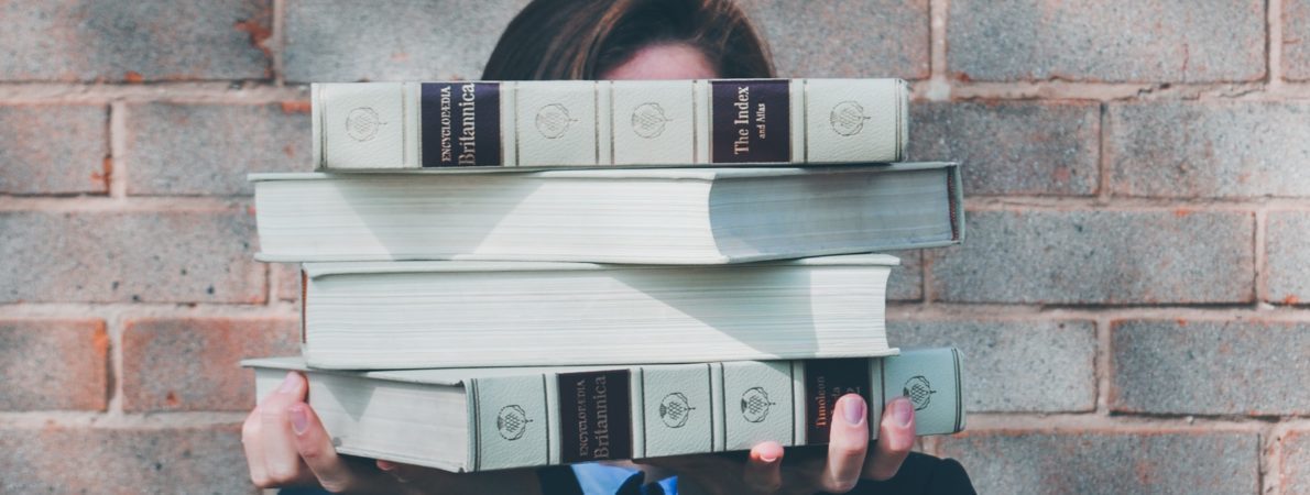 A person holding a pile of books in front of their face