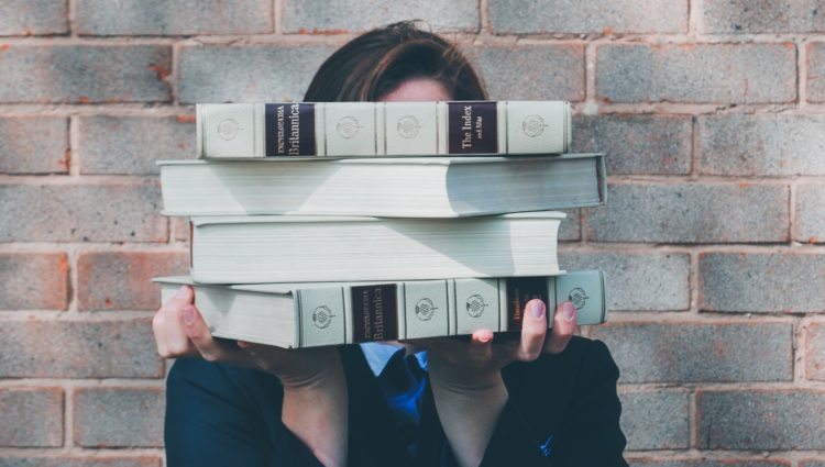 A person holding a pile of books in front of their face